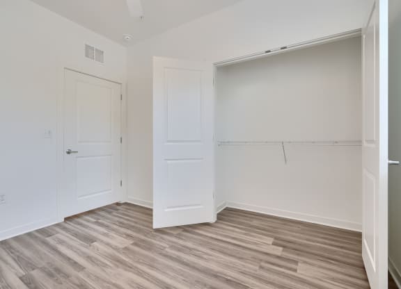 a bedroom with white walls and wood flooring and a closet