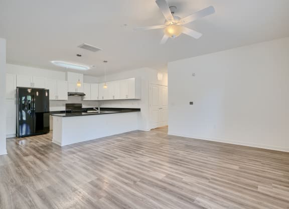 an empty living room and kitchen with a ceiling fan