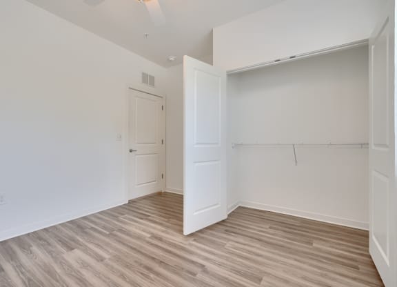 a bedroom with white walls and wood flooring and a closet