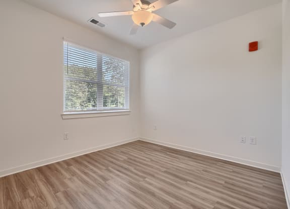 an empty bedroom with a ceiling fan and a window