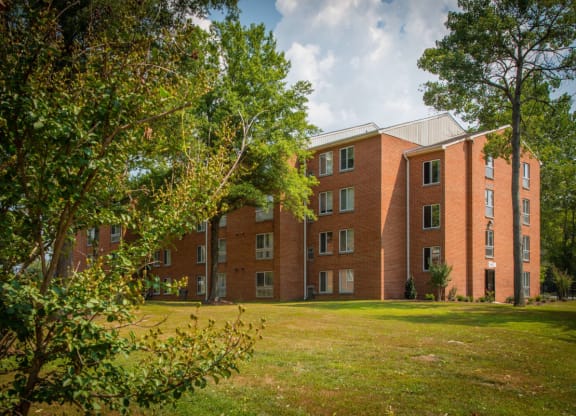 a large brick building with a green lawn and trees