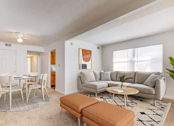 A living room with a white table and chairs, a grey couch, and a brown ottoman.