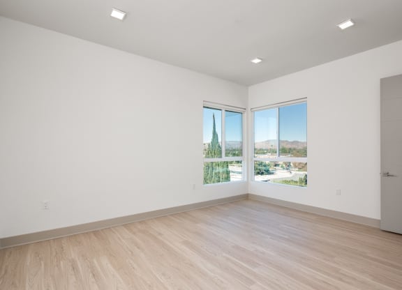 a living room with white walls and wooden floors and large windows