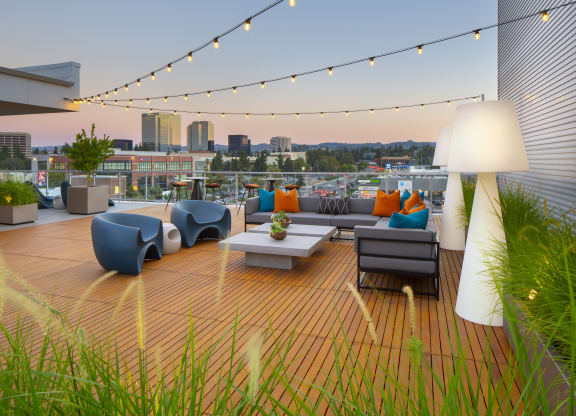 a roof deck with couches and chairs and a city in the background