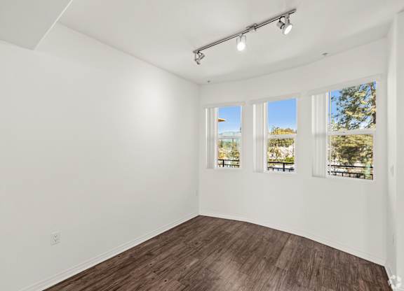A room with white walls and wooden flooring with three windows.
