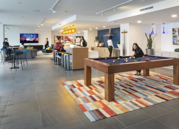 1-Bedroom Apartments in Woodland Hills, CA - The Q Variel Apartments -  Club House by the Pool with Vinyl Flooring, Plush Couches, Bar Stools, Wall-Mounted TVs,  Modern Light Fixtures, a Community Kitchen, and a Pool Table