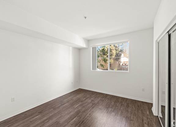 A room with a window showing a view of trees and a wooden floor.