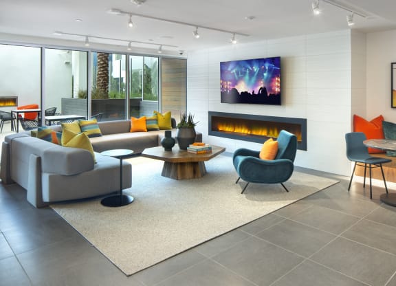 Studio Apartments for Rent in Woodland Hills, CA - The Q Variel Apartments - Clubhouse with Vinyl Flooring, Plush Couches, Tables, Wall Mounted TV, a Fireplace, Modern Light Fixtures, and Floor-to-Ceiling Windows