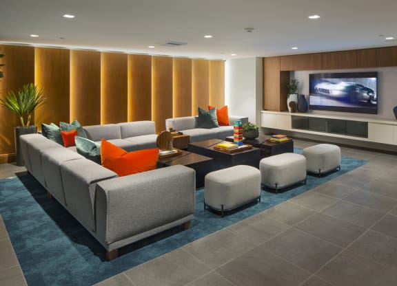Studio Apartments in Woodland Hills, CA - The Q Variel - Media Room with Large Comfortable Couches, Wooden Tables Equipped with Books and Games, a TV, and Modern Décor