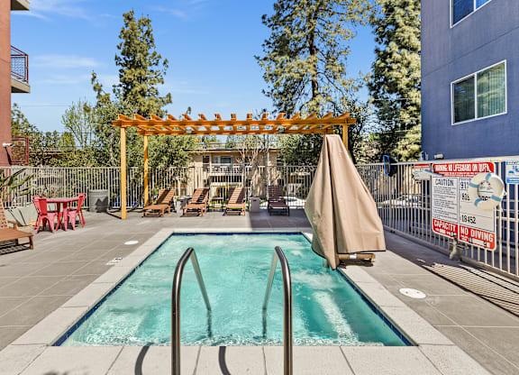 A pool area with a wooden pergola and lounge chairs.