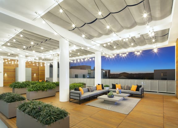 Woodland Hills, CA Apartments - The Q Variel - Penthouse Rooftop with Sofas, Plant Beds, String Lights, Wood-Style Floors and Walls, a TV, and City Views