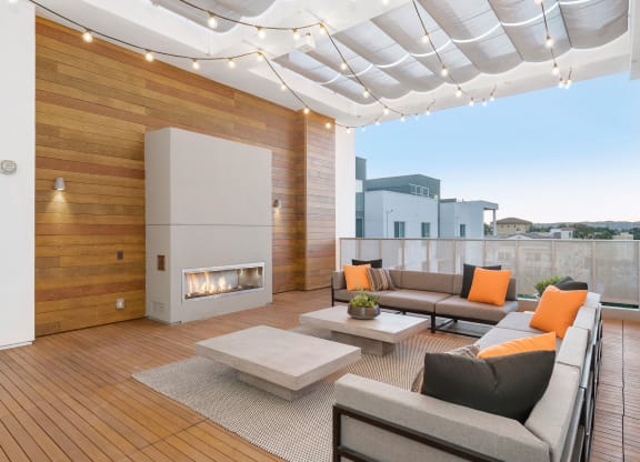 Two Bedroom Apartments in Woodland Hills, CA - The Q Variel - Outdoor Lounge with Couches, a Fireplace, Coffee Tables, String Lights, and City Views