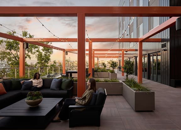 Two women are sitting on a couch under a pergola.
