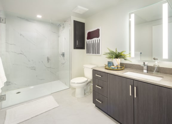 Studios in Woodland Hills, CA - The Q Variel - Bathroom with Quartz Countertops, Wood-Style Cabinets, a Shower with Marble Walls, and Tile Hard-Surface Flooring