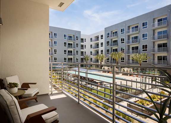 A balcony with chairs and a table overlooks a pool and buildings.