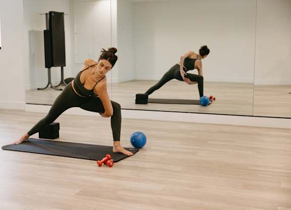 A woman is doing a workout with a blue ball and red dumbbells.