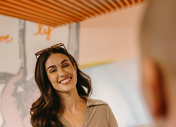 A woman in a beige shirt is standing behind a counter and smiling.