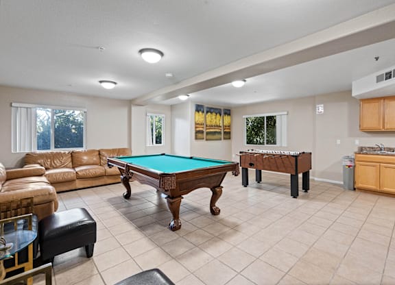 A billiard table is in the middle of a room with a couch and a chair.