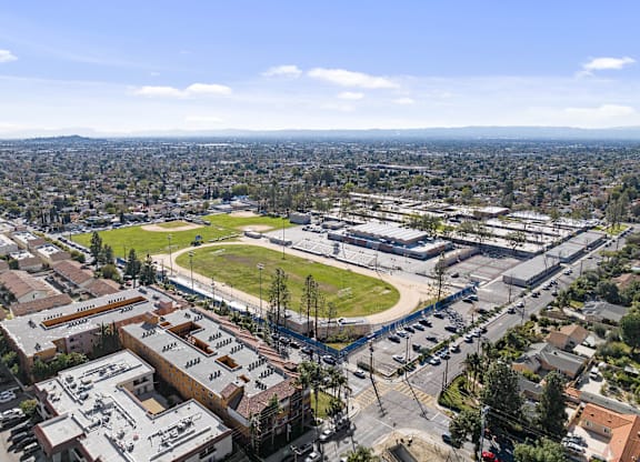 A view of a city from a high vantage point with buildings, a parking lot, and a green field.