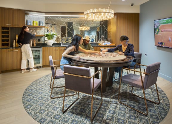 a round table with three people sitting around it and a woman standing in a kitchen in the