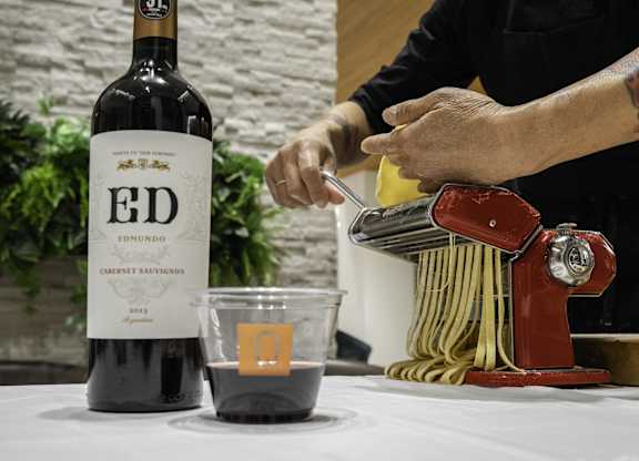 A bottle of Ed Emundo 2013 Cabernet Sauvignon is on a table next to a cup of wine and a pasta maker.