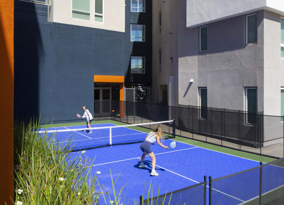 two women playing tennis on a blue court in front of a building