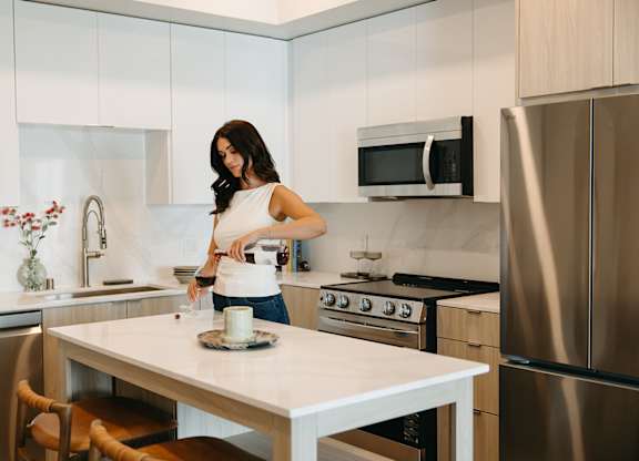 A woman is standing in a kitchen with a white table and a stainless steel refrigerator.
