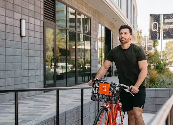 A man is riding a bicycle with a basket on the sidewalk.