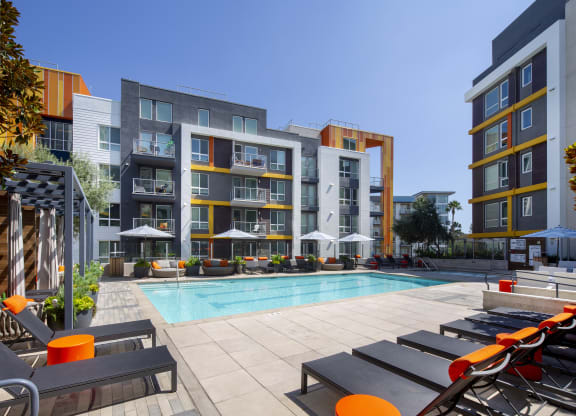 a pool with lounge chairs in front of an apartment building