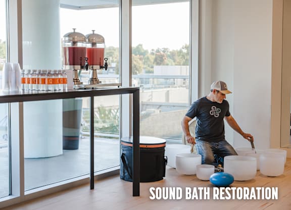 A man is working on a sound bath restoration setup in a room with large windows.