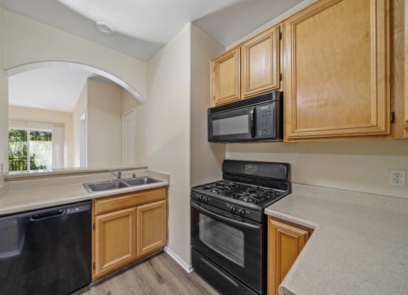 a kitchen with wooden cabinets and black appliances at The Village Apartments, Van Nuys, 91406