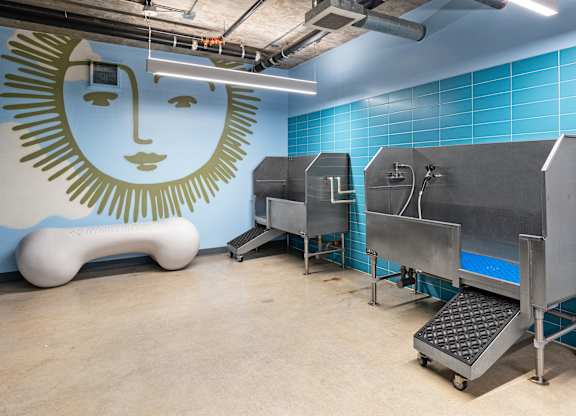A large industrial machine sits in a room with a blue tiled wall and a mural of a face.