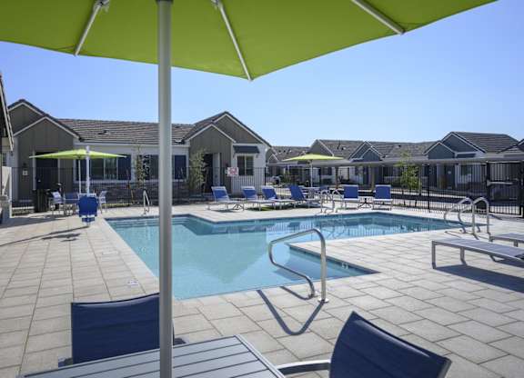 a swimming pool with chairs and umbrellas in front of a house at Village of Chandler Apartments, Chandler, Arizona