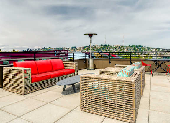 A roof top patio with a red couch, a wicker table, and a wicker ottoman