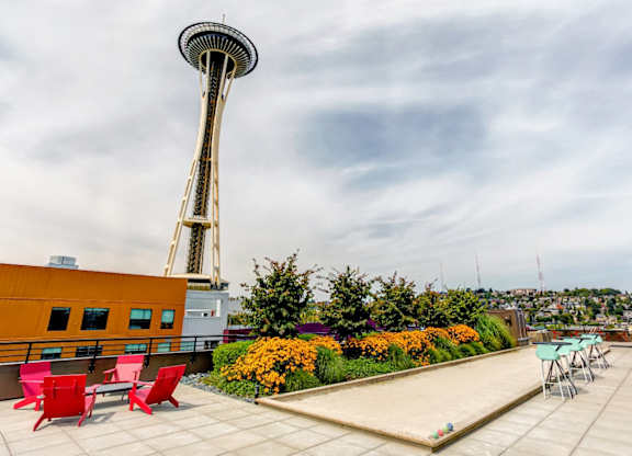 A rooftop patio with red chairs and a pool table with the Seattle Space Needle in the background