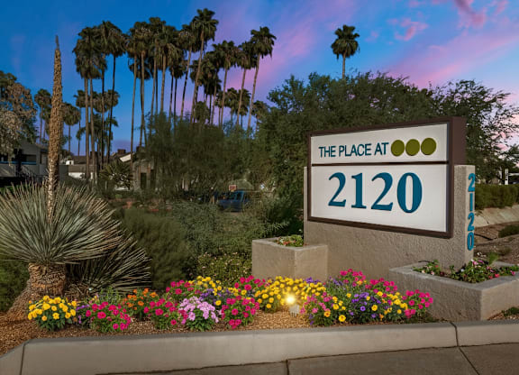 A sign that says "The Place at 2120" is in front of some plants and trees.