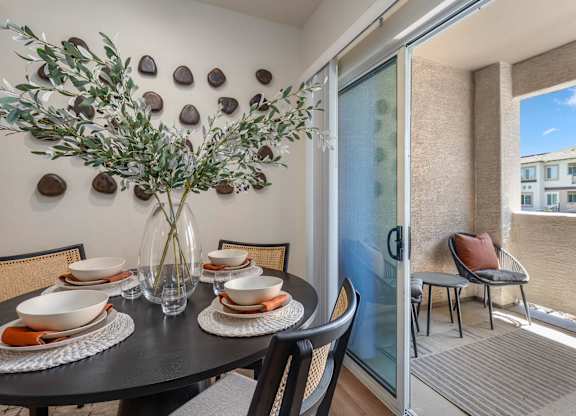 A dining table with chairs and a vase with a plant in it.