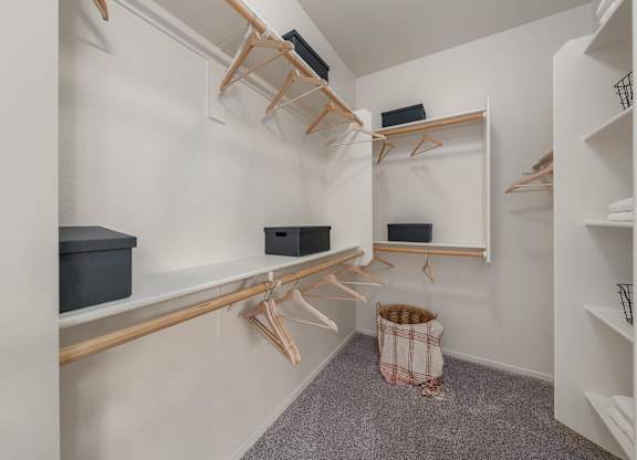 A walk-in closet with white shelves and wooden hangers.
