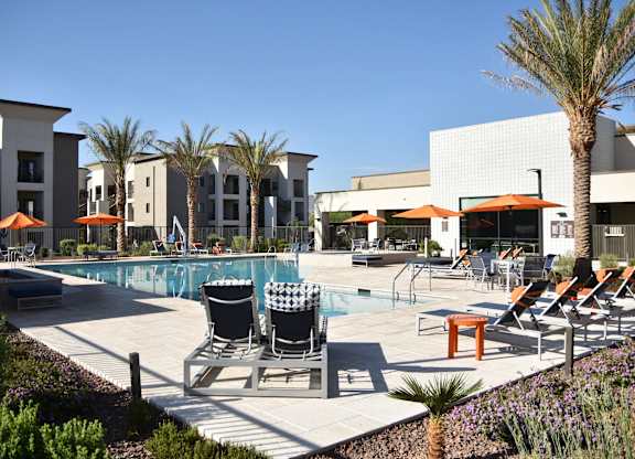 A pool area with chairs and umbrellas in front of a building.