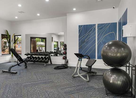 A gym with a variety of equipment including a rowing machine, a bench press, and a stability ball.