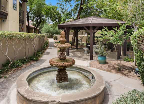 A fountain in the middle of a courtyard with a gazebo in the background.