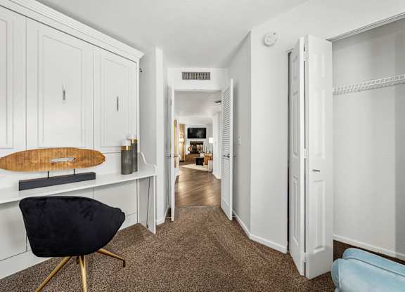 A black chair sits in front of a white cabinet with a wooden cutting board on top.