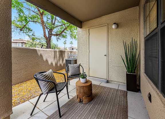 A patio with a chair, table, and potted plant.