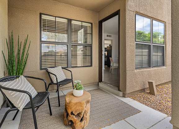 A patio with a chair, table, and potted plant.