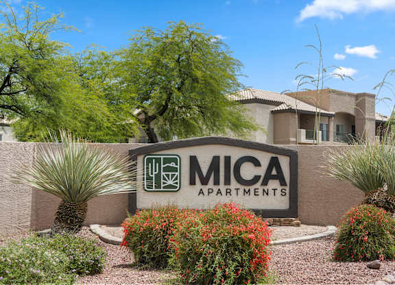 The image shows a sign for Mica Apartments surrounded by plants and trees.