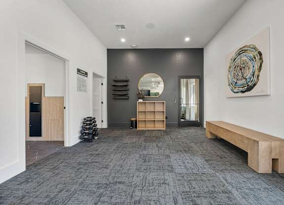A hallway with a bench, a mirror, and a painting on the wall.