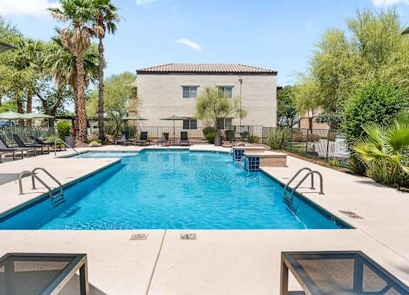 A swimming pool surrounded by palm trees and a building in the background.