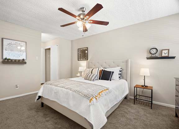 A bedroom with a bed, a ceiling fan, and a nightstand with a lamp.