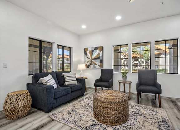 A living room with a dark blue couch, two chairs, and a woven ottoman.