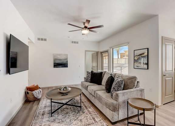 A living room with a grey couch, a coffee table, and a flat screen TV mounted on the wall.